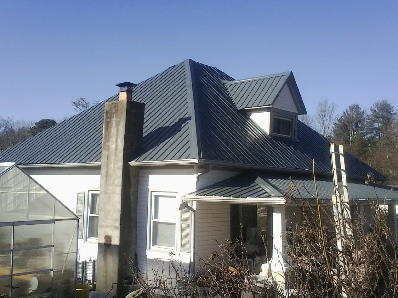 Dark blue standing seam metal roof on a white farmhouse with dormer — Slate & Tile Roof Repair by Roofing Brothers in Phelan