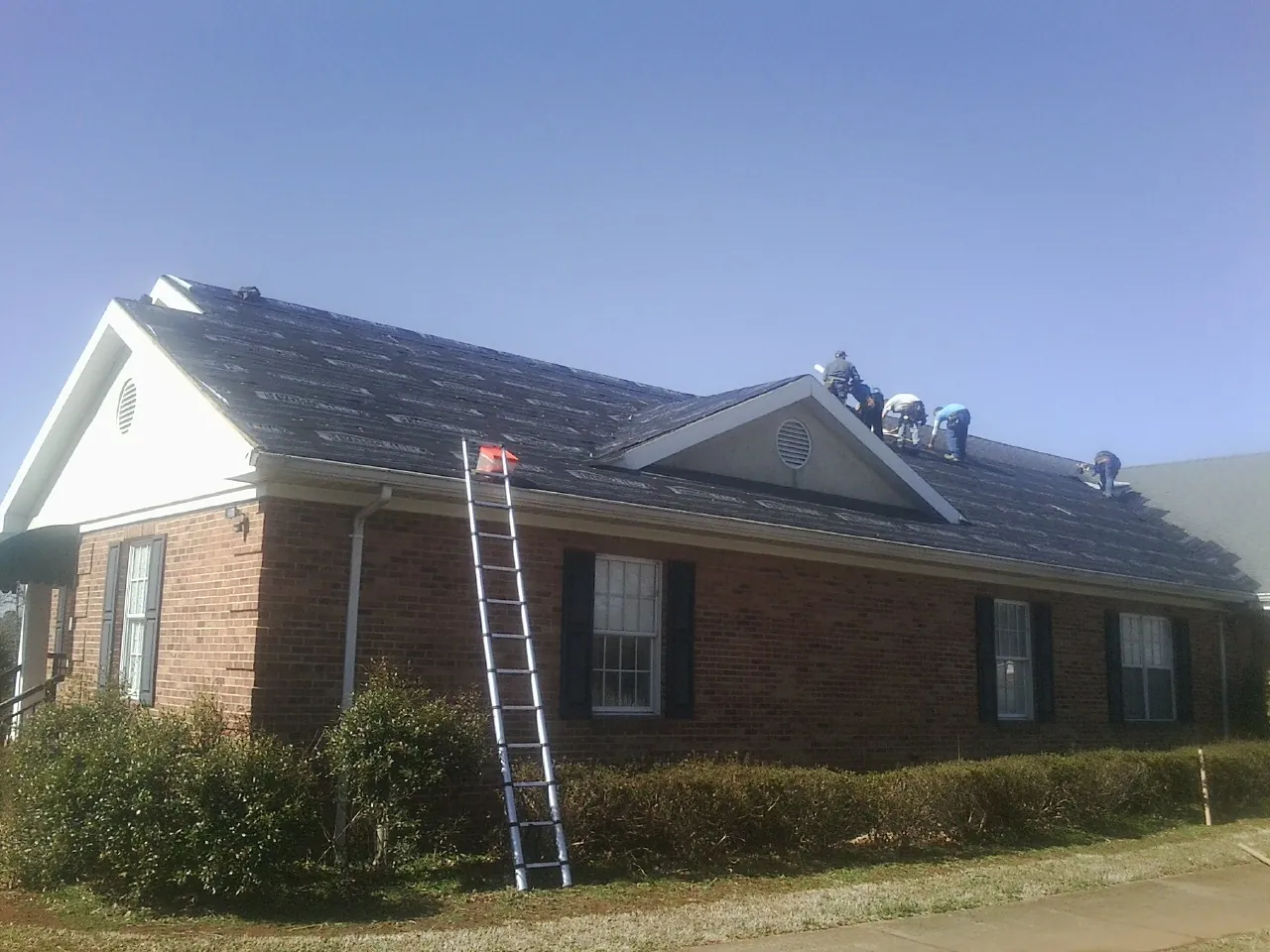 Crew tearing shingles off a brick ranch roof with a ladder set — Emergency Roof Repair work by our crew in Phelan