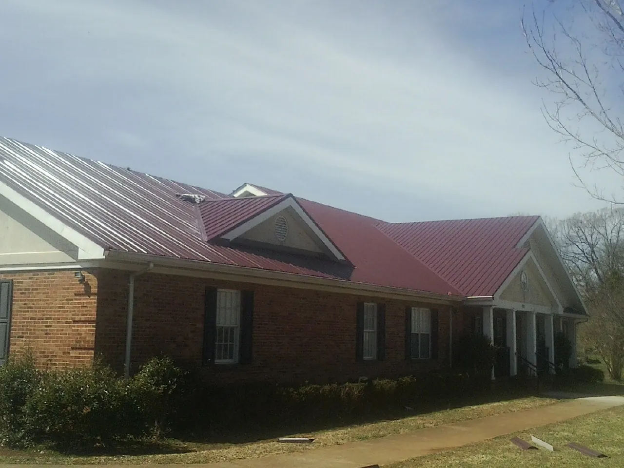 Red metal roof with gabled entries on a long brick building, from a Hail Damage Roof Repair job in Phelan