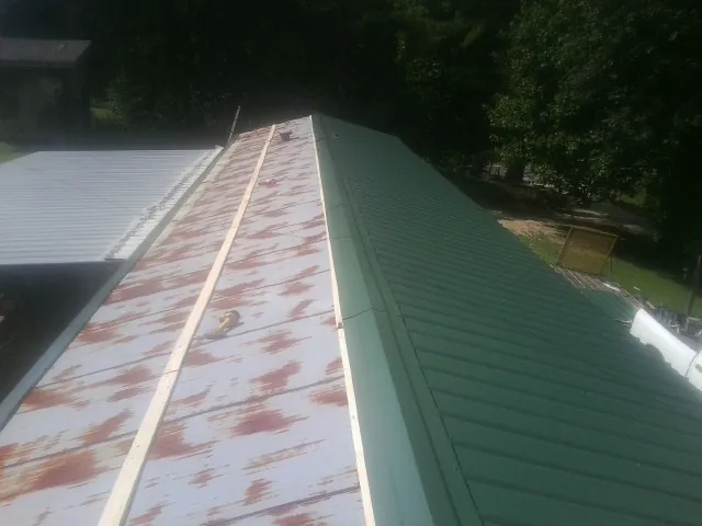 Old rusted panels beside newly installed green metal roofing — Wind Damage Roof Repair by Roofing Brothers in Phelan