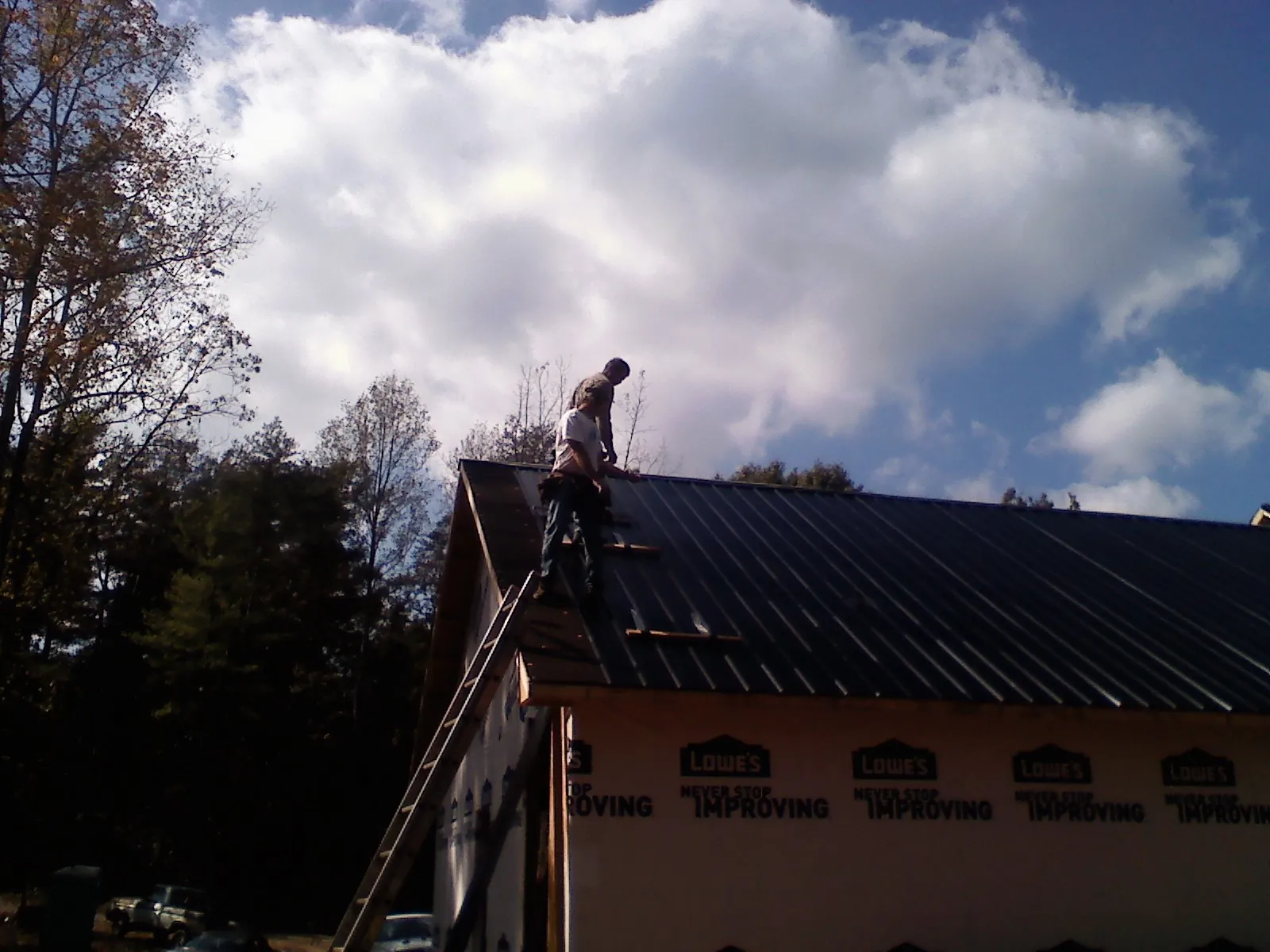 Roofer fastening dark metal panels high against a cloudy sky, from a Roof Inspection job in Phelan